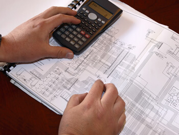 Engineer using a calculator while reviewing blue prints 